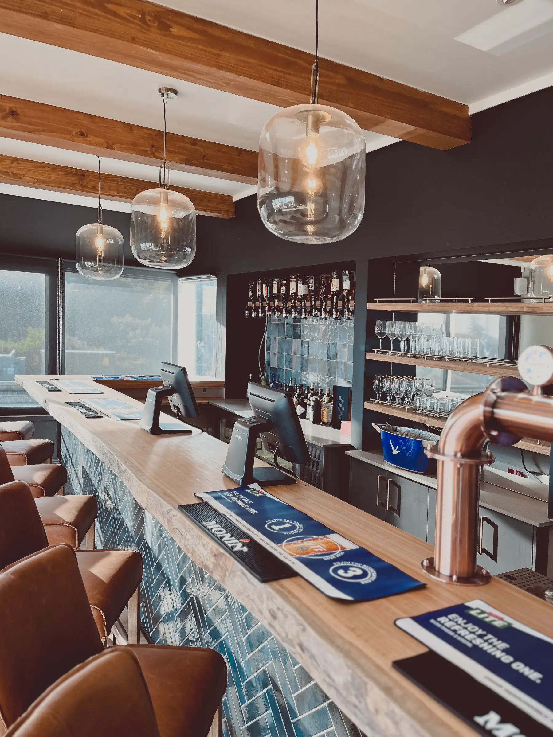 Renovated bar area with brown leather bar stools and stylish glass light fixtures.